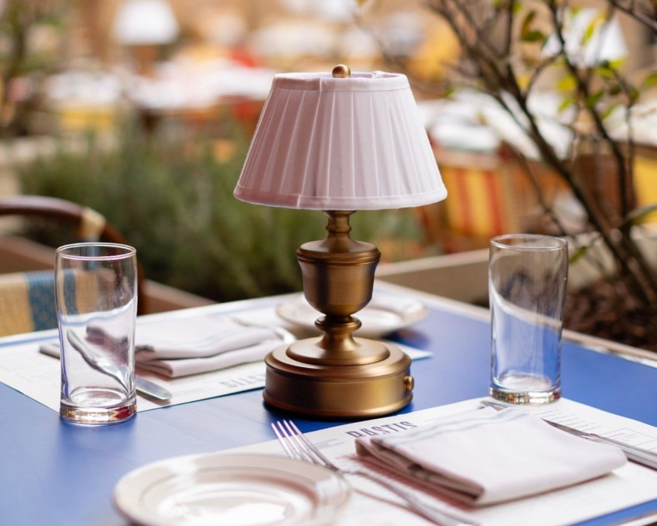 A charming outdoor dining scene from Pastis, a French brasserie in Nashville, featuring signature blue-topped tables and golden-brass lighting, curated by Luxe & Luna Boutique Spa as a top destination for a restorative, European-inspired afternoon