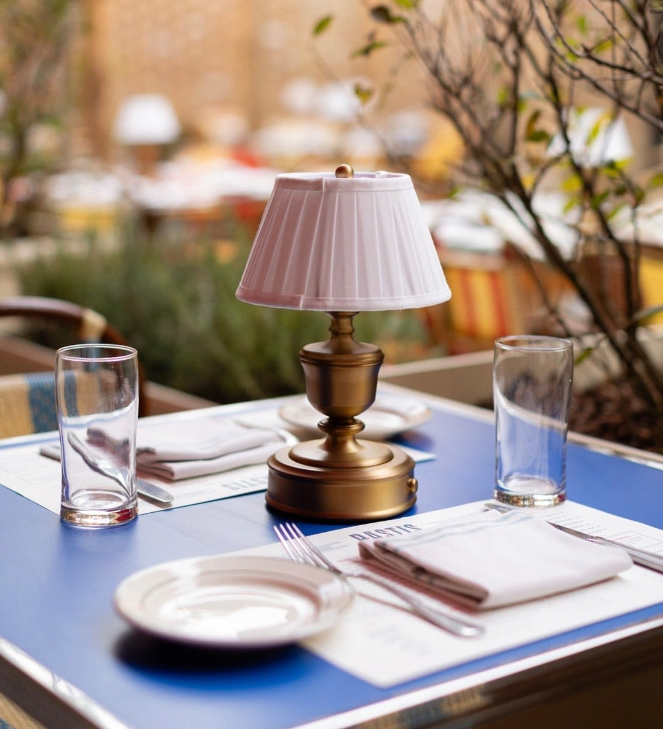 A charming outdoor dining scene from Pastis, a French brasserie in Nashville, featuring signature blue-topped tables and golden-brass lighting, curated by Luxe & Luna Boutique Spa as a top destination for a restorative, European-inspired afternoon