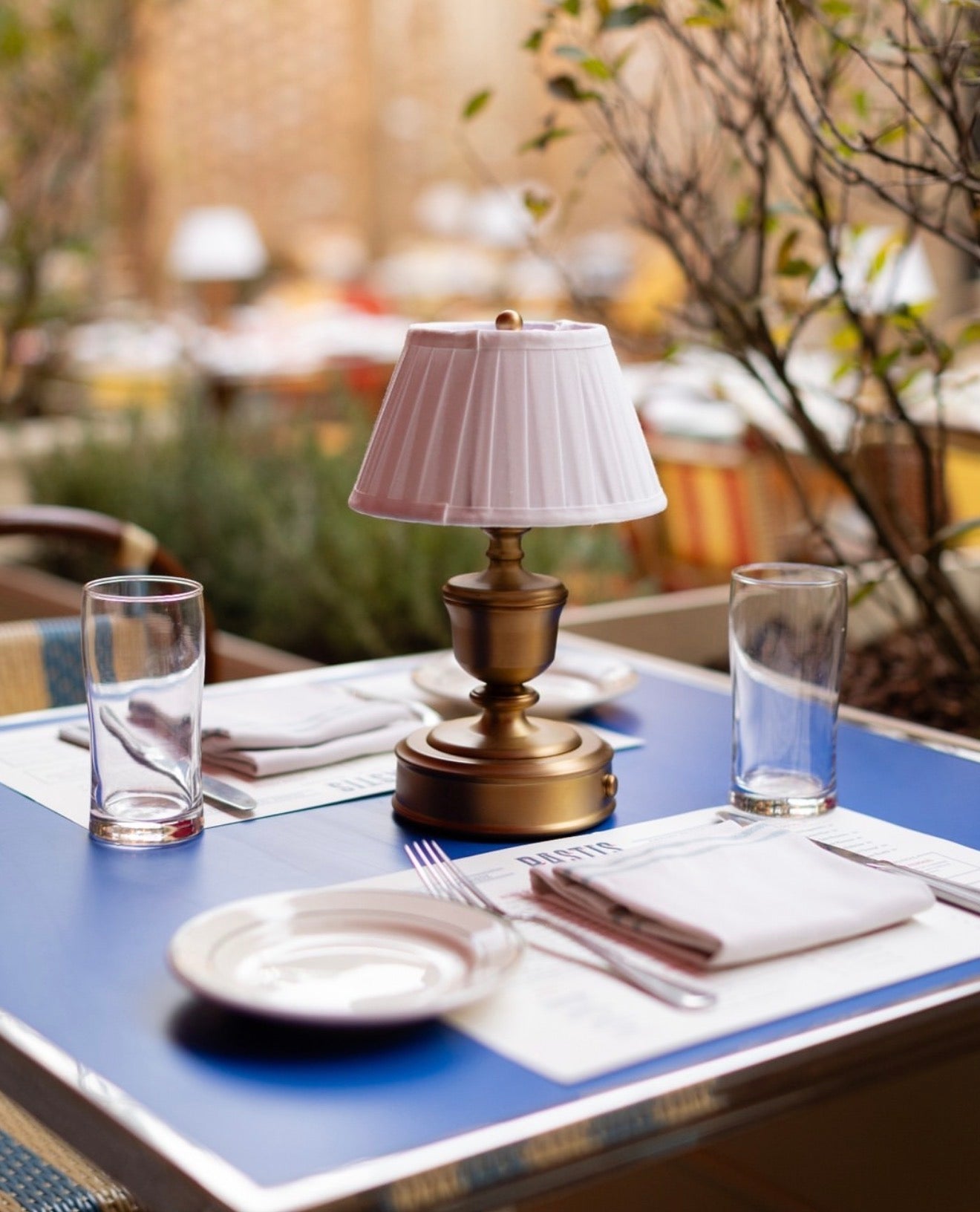 A charming outdoor dining scene from Pastis, a French brasserie in Nashville, featuring signature blue-topped tables and golden-brass lighting, curated by Luxe & Luna Boutique Spa as a top destination for a restorative, European-inspired afternoon